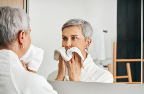 Mature adult woman wiping her face after morning routine in the bathroom