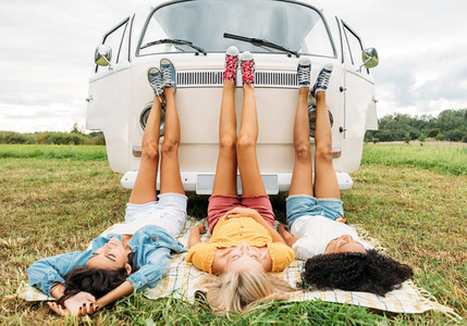 Three women lying on a blanket in front of a camper van