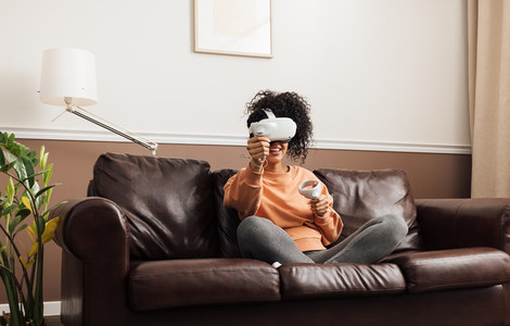 Woman in casual clothes relaxing at home  Mixed race female having fun while playing video games with VR set