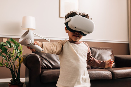 Little boy wearing VR glasses and holding a controller while standing in living room