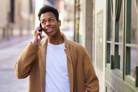 Young black man talking on the phone while walking down the street