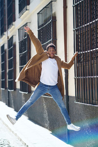 Young black man jumping holding on to a window grille in the street
