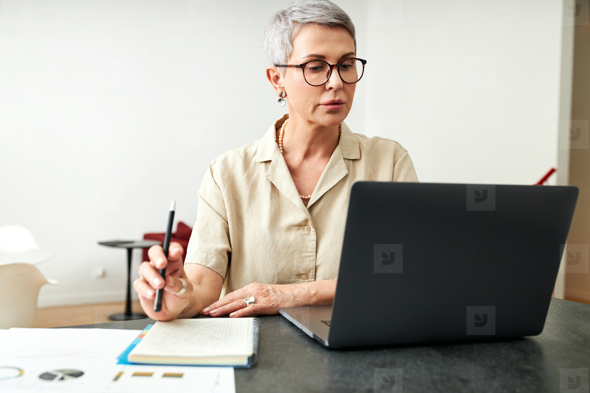 Mature woman looking on laptop screen holding a pen