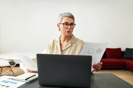 Mature woman wearing eyeglasses holding documents in hands while sitting at home