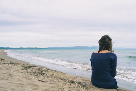 girl sitting on the sand on the shore of the beach looking at the horizon of the sea