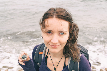 girl with medium brown hair with blue eyes looking at the camera holding a shell