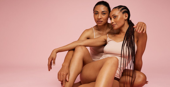Two female models sitting over pink background