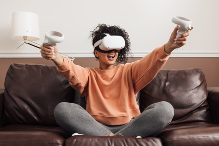 Cheerful mixed race woman sitting on a couch with VR headset