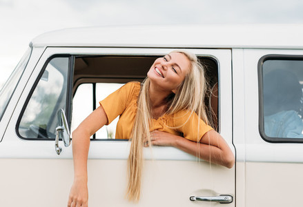 Happy blond woman with closed eyes sitting on a driver seat enjoying a road trip