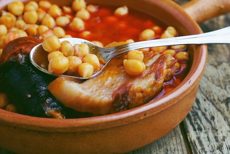 Chickpeas, sausage and bacon in a crockpot by wooden spoon and f