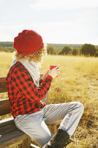 A young woman from behind in red plaid shirt with a wool cap and