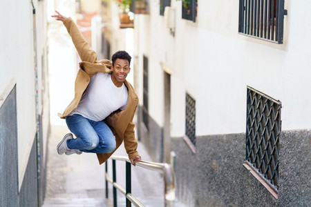 Young black man jumping for joy over a handrail in the street