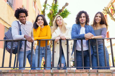 Multi ethnic group of friends gathered in the street leaning on a railing