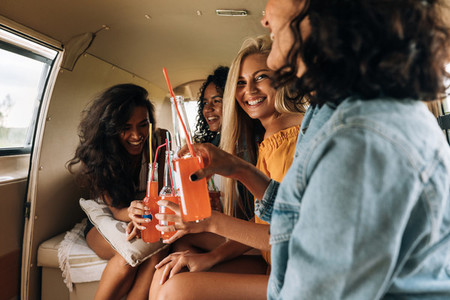 Four women drinking cocktails in camper van enjoying summer vacation