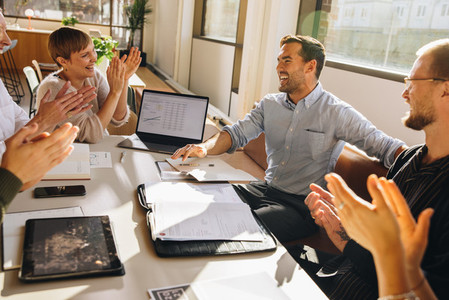 Creative team clapping for young executive in meeting
