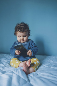 Little baby playing with a smart phone in a blue room