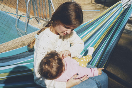 Young woman caring her baby sitting on a hammock