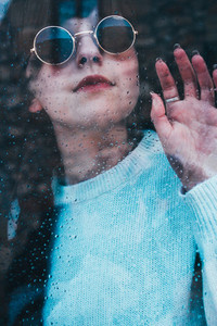 Sad woman alone in her home looking through a window in a rainy