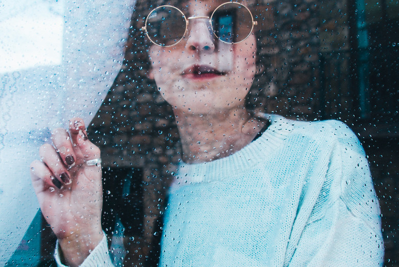 Sad woman alone in her home looking through a window in a rainy