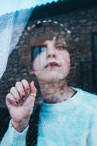 Sad woman alone in her home looking through a window in a rainy