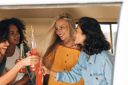 Four women toasting with bottles while sitting in camper van