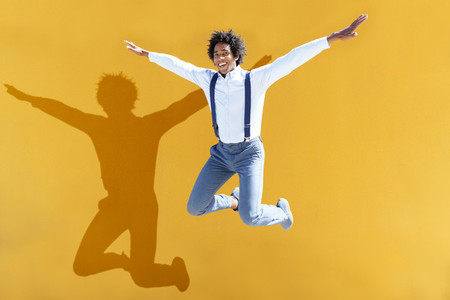 Black man with afro hair jumping on a yellow urban background