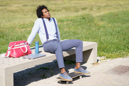 Black man with afro hair taking a coffee break sitting on a park bench