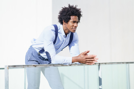 Attractive black businessman with afro hair  resting on a railing of his office building