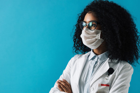 Confident female doctor wearing eyeglasses and protective mask looking away over blue background