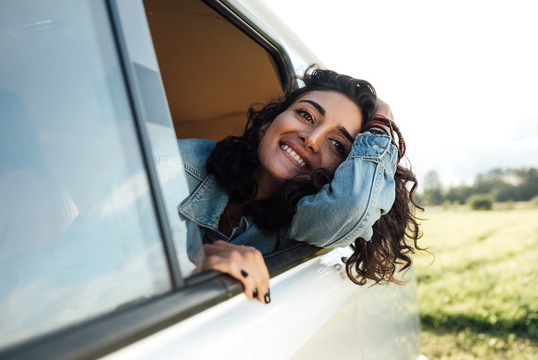 Attractive young woman enjoying road trip  Smiling female looks out of van window