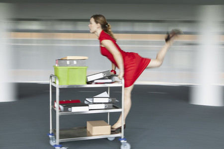 Carefree businesswoman pushing and riding office cart