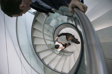 Businessman watching colleagues talk at bottom of spiral staircase