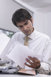 Confused businessman reviewing paperwork in office