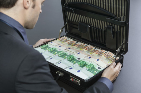 Businessman looking at briefcase full of cash Euros