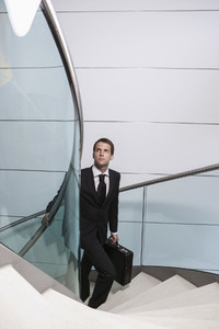 Businessman with briefcase looking up ascending spiral staircase