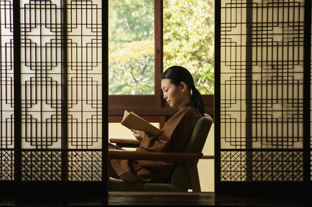 Serene young woman reading book behind patterned shoji doors