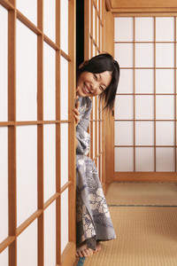 Portrait happy playful young woman in kimono peering from behind shoji door