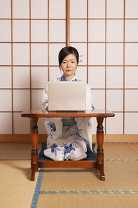 Young woman in kimono working at laptop at shoji door