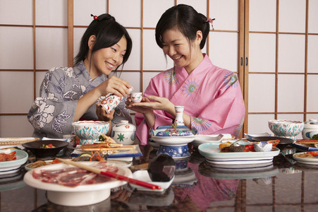 Happy young Japanese women in kimonos drinking tea with lunch