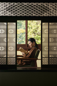 Young woman reading book in ornate shoji doorway