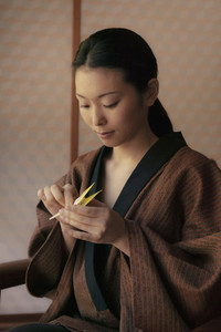 Beautiful young woman in robe making origami paper crane