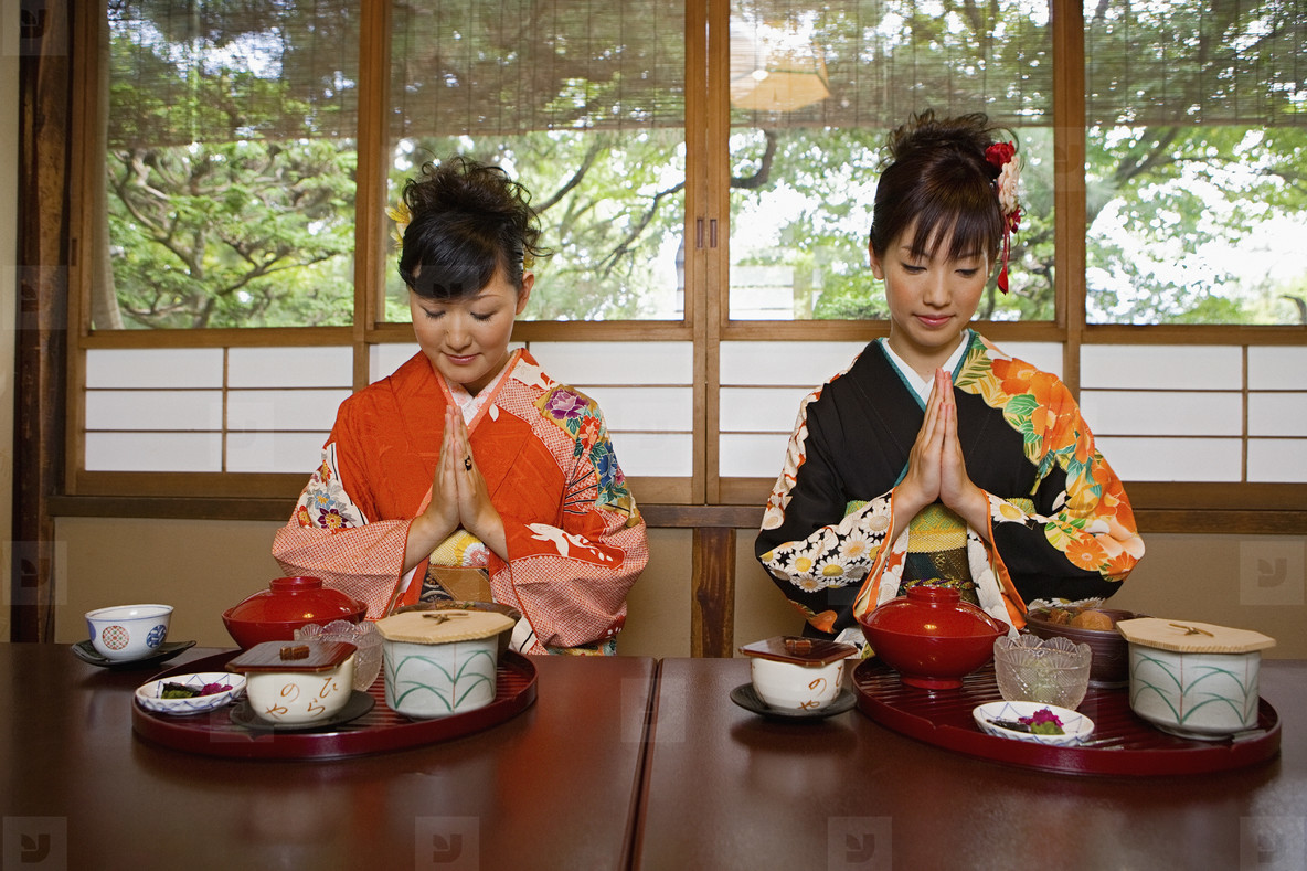 Young women in kimonos praying over lunch in restaurant