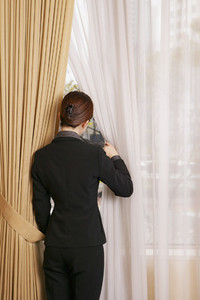 Businesswoman looking out window between curtains