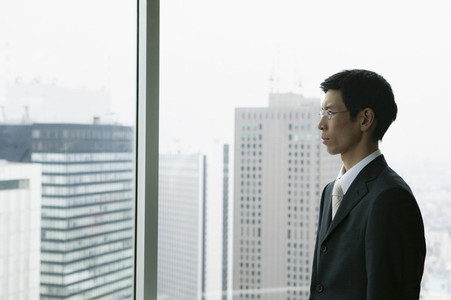 Businessman looking out urban highrise office window
