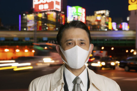 Portrait confident businessman in face mask in city at night Tokyo Japan
