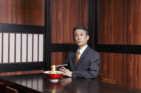 Businessman with levitating chopsticks and noodles in restaurant