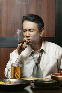 Businessman smoking cigar at lunch in restaurant