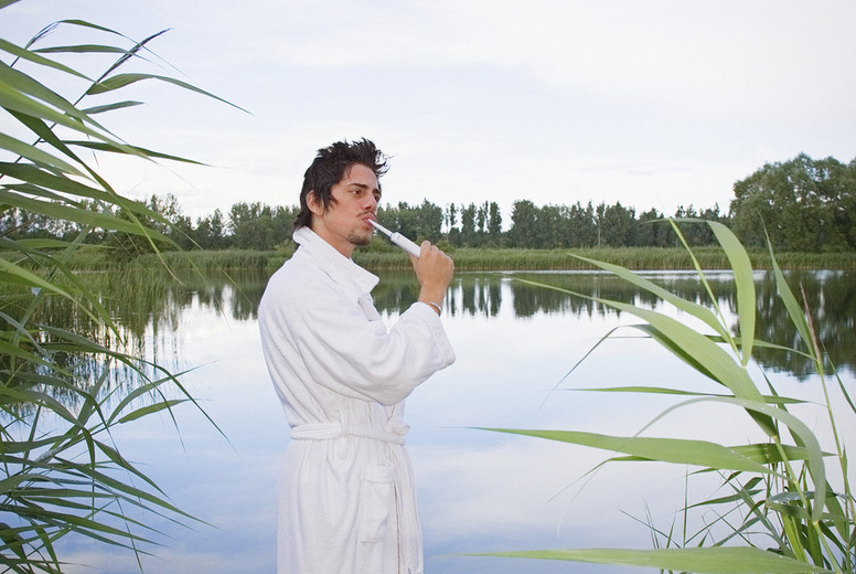 Man in bathrobe brushing teeth at tranquil lake