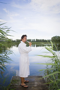 Man in bathrobe brushing teeth at tranquil lake