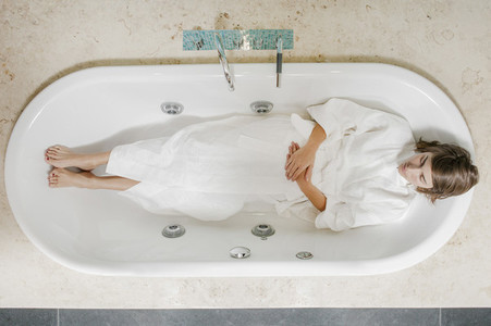 Serene young woman in bathrobe laying in empty bathtub